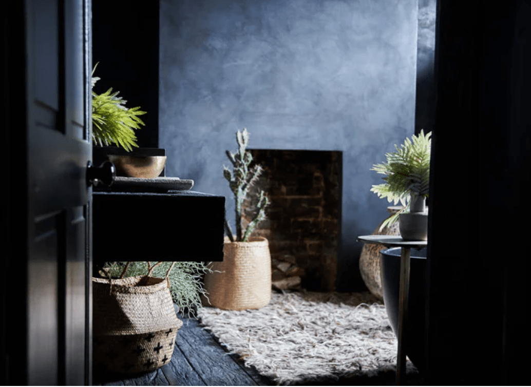 stylish dark bathroom in the home of designer Abigail Ahern with moroccan plaster tadelakt walls, lots of green artificial plants a shaggy wool rug