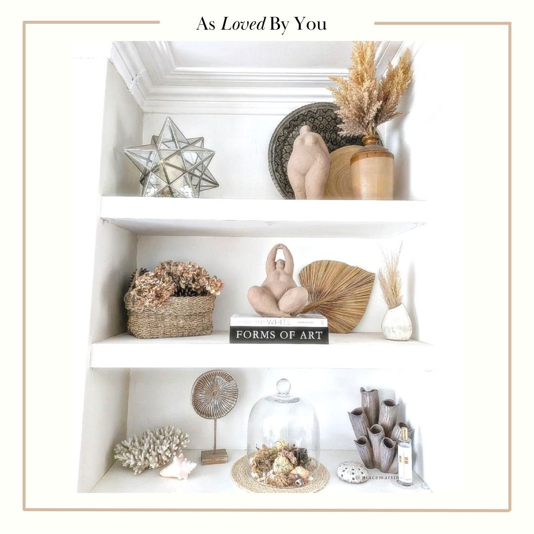 A stylised image of various home accessories including some female sculptures, book and faux flowers arranged on white shelves.