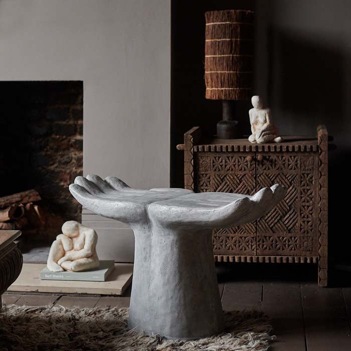 White, textured stool in the shape of two hands next to a fireplace