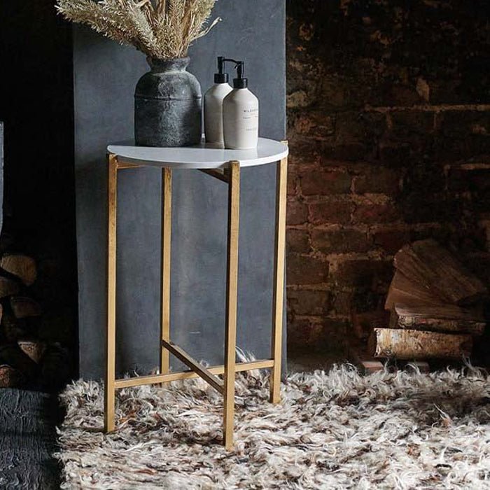 A round side table with gold metal legs and frame, topped by white faux marble table top.
