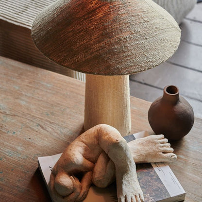 Beige woven silk table lamp on a wooden coffee table, styled with a cream female sculpture.
