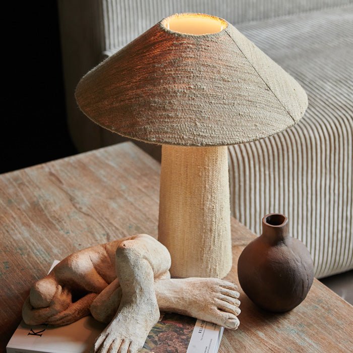 Table lamp with tall cylindrical base leading to cone shaped shade, covered in creamy beige woven fabric. Luxury lighting design for a stylish home. 