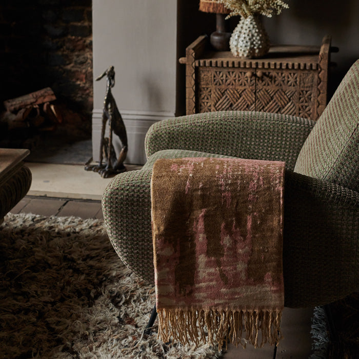 Pink patterned throw with tassels draped over the arm of an armchair