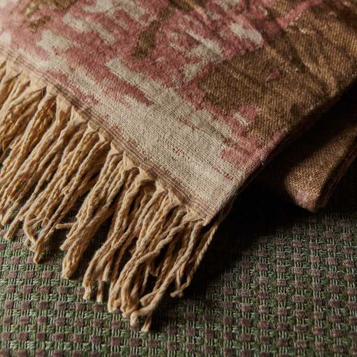 Brown tasseled throw with a pink and brown pattern lying on an armchair
