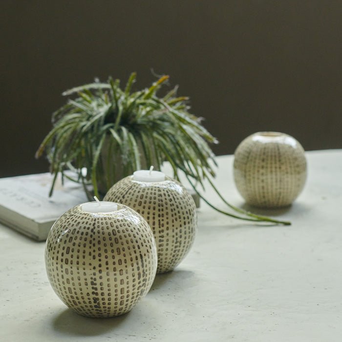 Three round cream candleholders with black dots sat on a cream coffee table