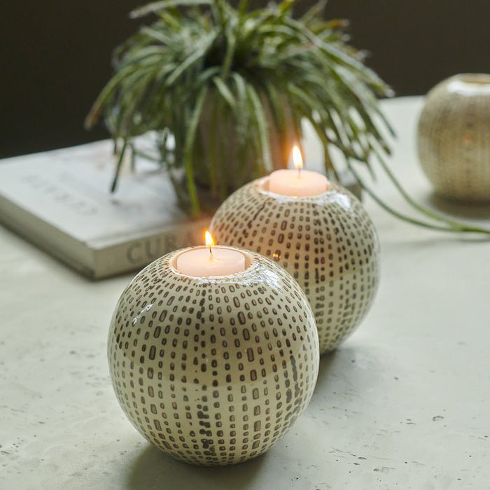 Two lit tea lights in two spherical cream candleholders with a black dotted pattern