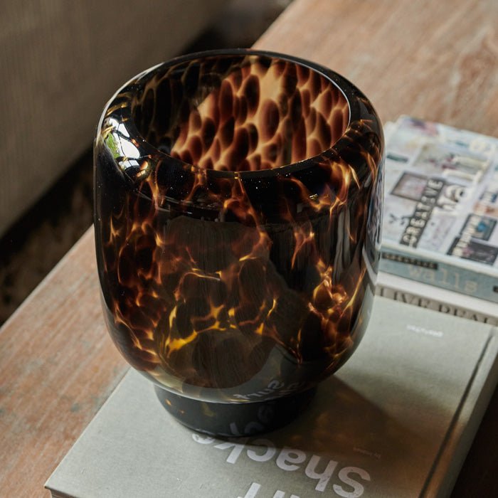 Round amber glass vase with brown spots sat on a large book on a wooden coffee table