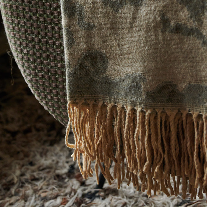 Brown and grey patterned throw with tassels draped down the side of an armchair