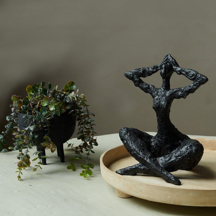 Matte black resin sculpture of seated figure.