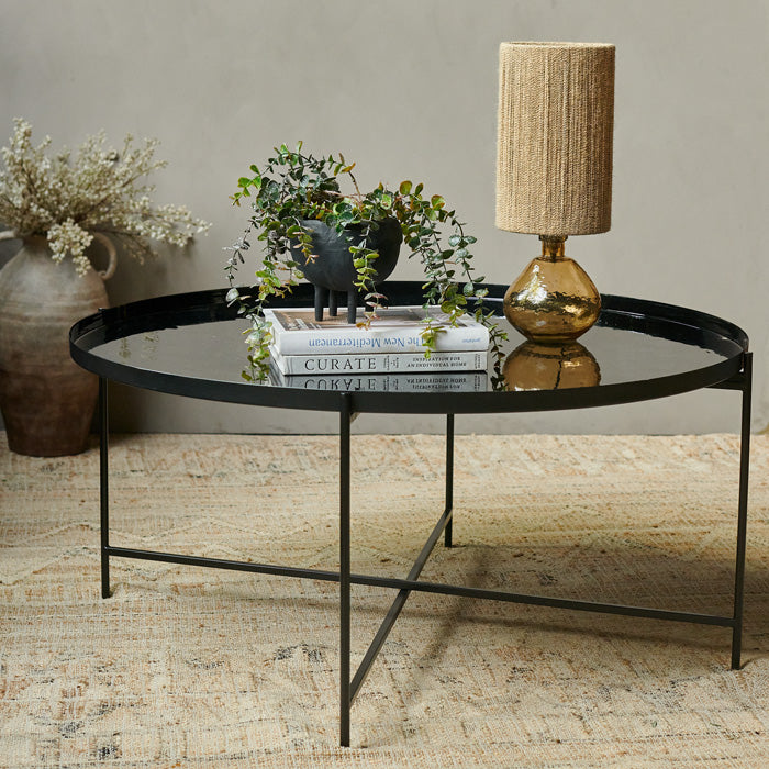 Round black enamel tray table with an amber glass table lamp and a stack of books on top
