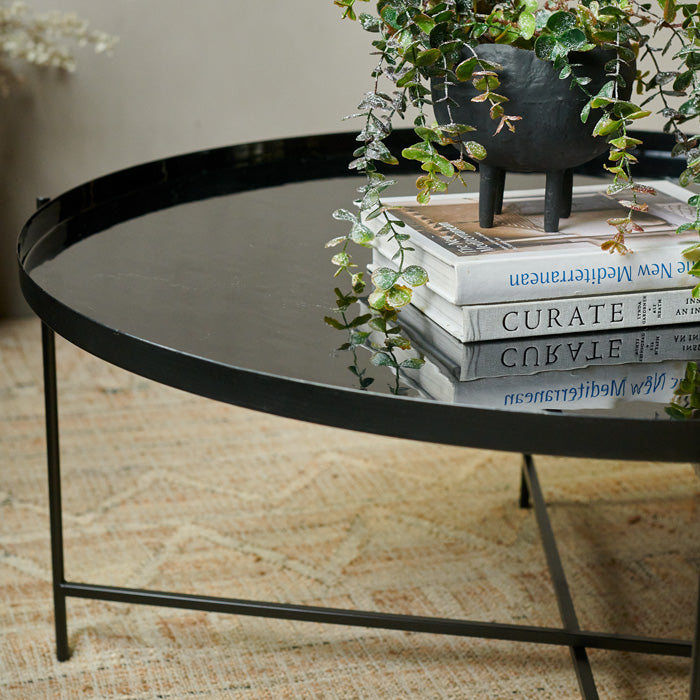 Black enamel tray table with a stack of two books and a black pedestal vase on top
