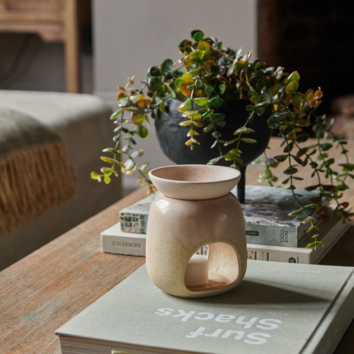 The Thea Oil Burner, a cream coloured ceramic oil burner sat on a book on a wooden coffee table.