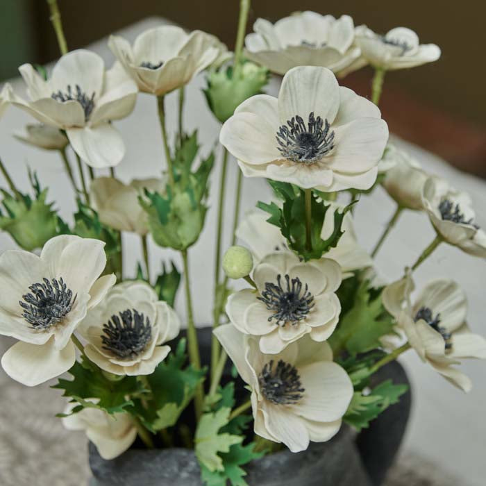 Artificial anemone flowers with cream petals, dark grey centre, and green leaves.