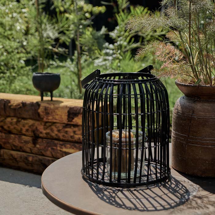 Round, black bamboo lantern with a pillar candle placed in its glass holder