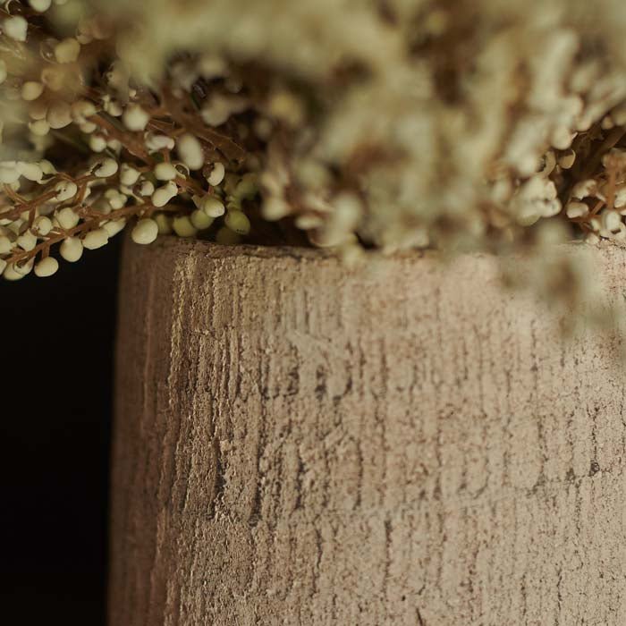 Textured surface of a grey vase filled with white faux foliage