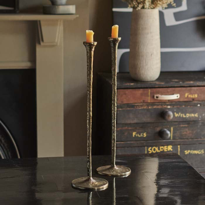 Two tall brass candlestick holders with yellow candles sat on a black dining table