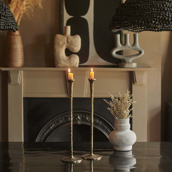 Two tall brass candleholders placed on a black dining table