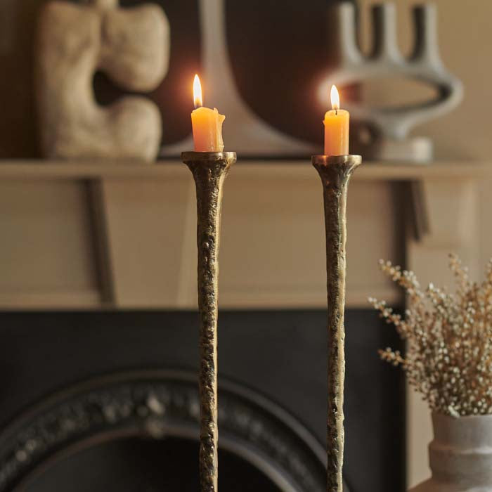Two burning yellow candles placed in tall, brass candleholders