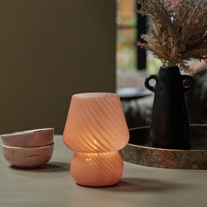 A small battery operated table lamp in a soft coral colour with swirling lines and a mushroom style.