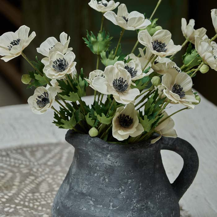 Cream anemone faux flowers in grey stoneware jug.
