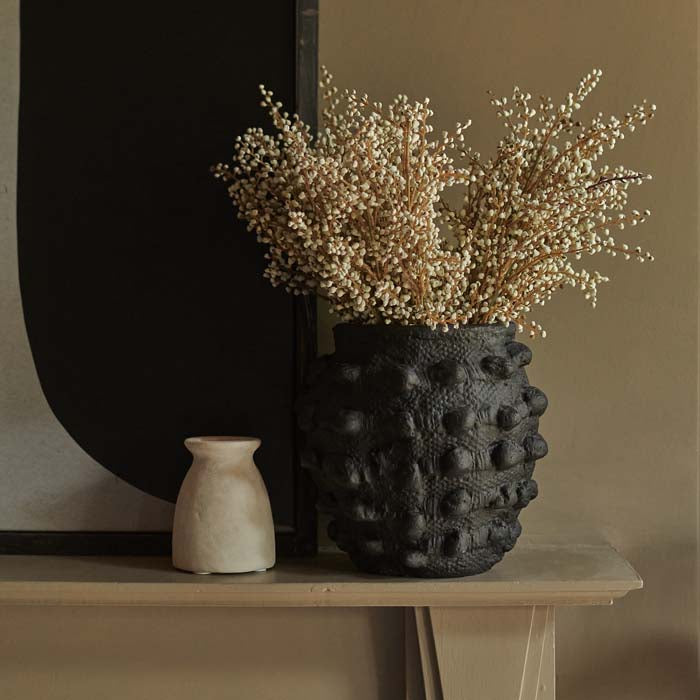 Black bobble textured vase sat on a mantle with a large artwork behind