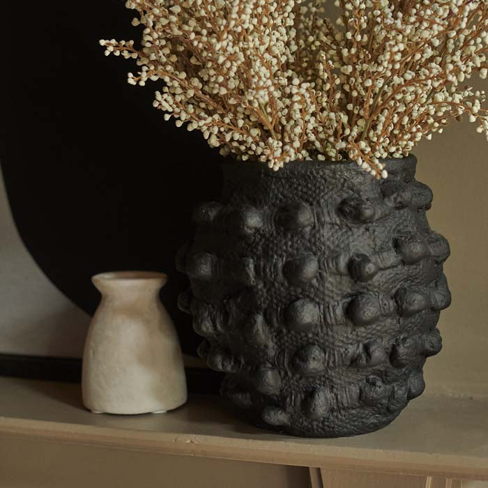Black concrete bobble vase next to a cream bud vase sat on a mantle