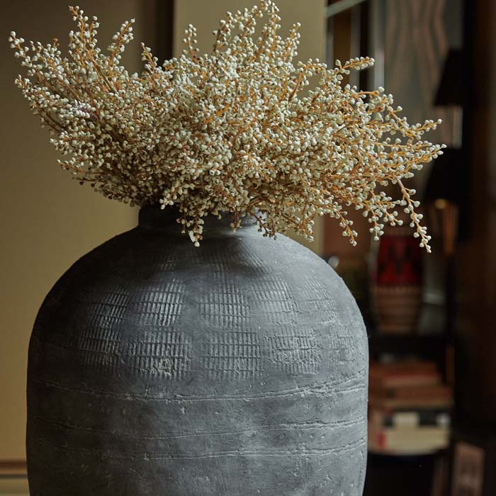 Rustic grey cement vase with imprinted grid textures, filled with artificial white heather flowers.