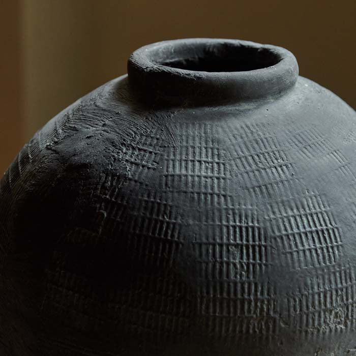 Imprinted grid texture and rustic finish on grey cement vase.