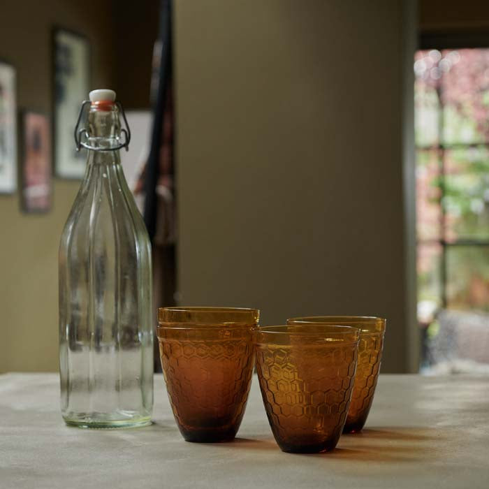 Four textured amber glass tumblers next to a clear water bottle