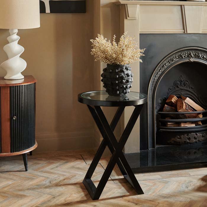 Round black side table with a glass top sat on a parquet wooden floor
