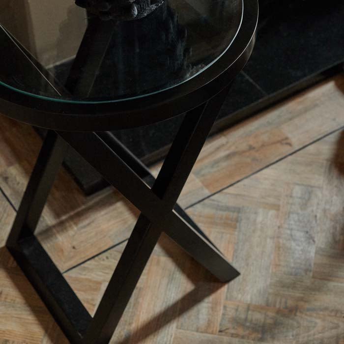 Black cross frame of a side table sat on a parquet wooden floor
