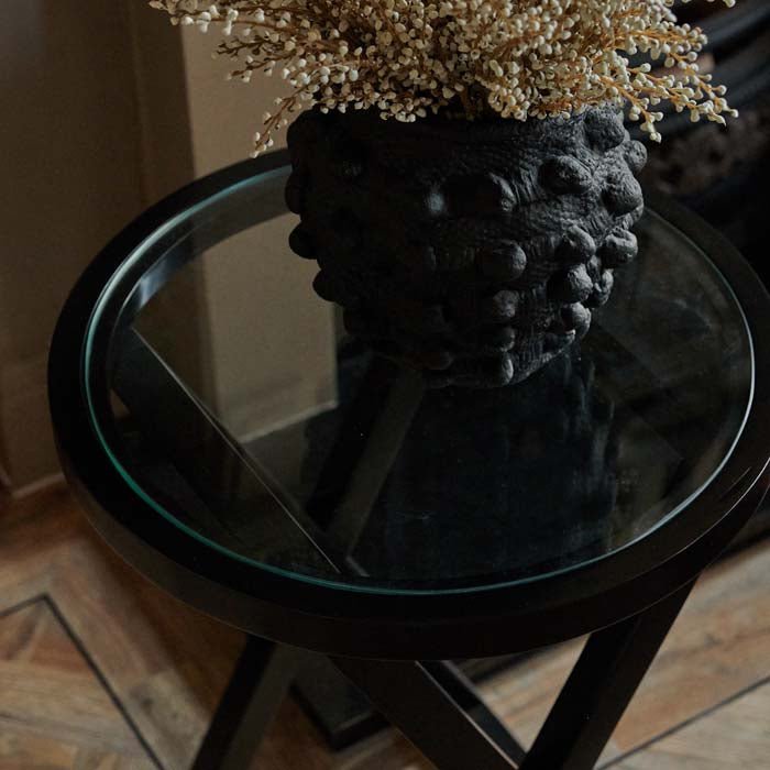 Round black framed side table with a glass centre and a black vase on top