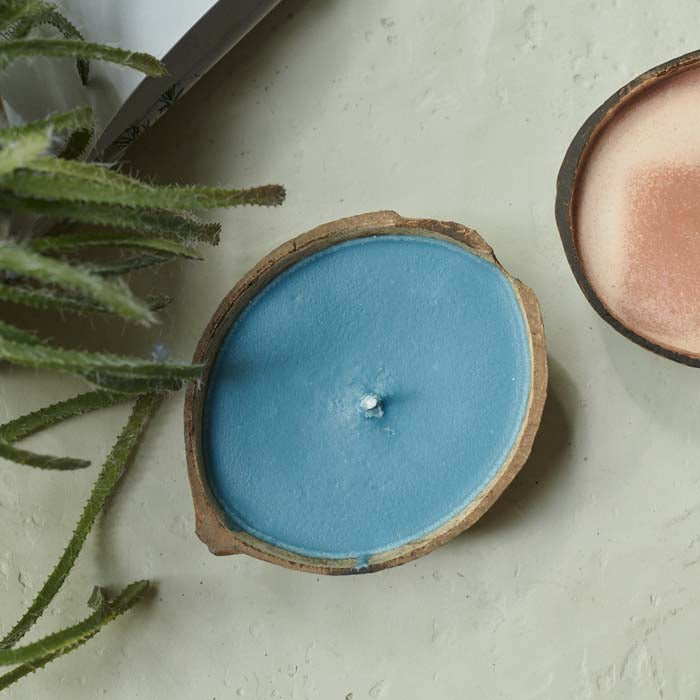 Blue scented candle placed in half a coconut shell sat on a cream coffee table