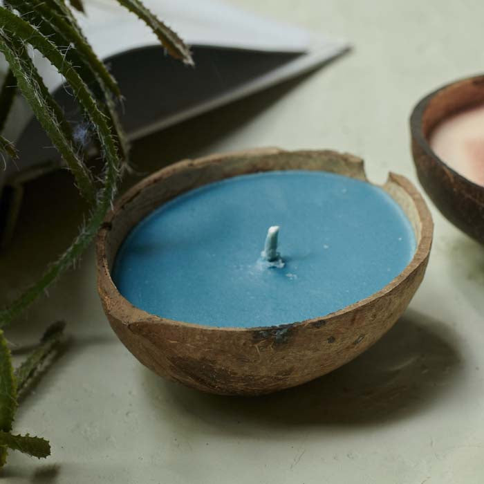 Blue coloured scented candle placed in a coconut shell sat on a coffee table