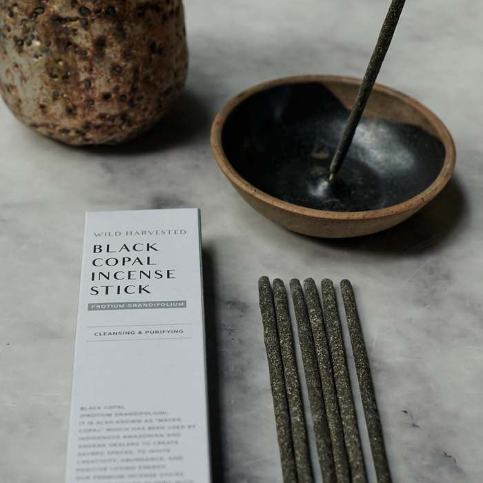 6 incense sticks lying flat next to its grey boxed packaging and a round incense holder