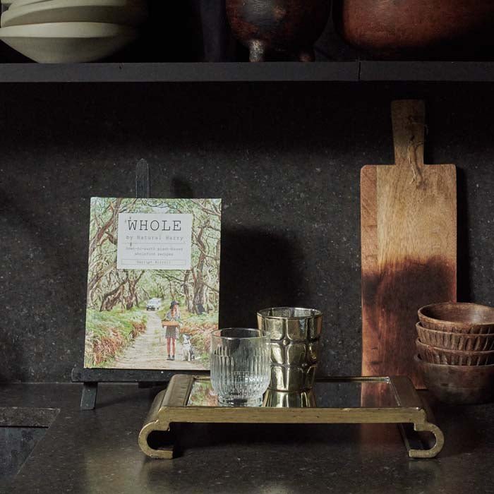The Bletchley Mirrored Tray, a rectangular tray with a curved pedestal base sits on a black work surface next to a book.