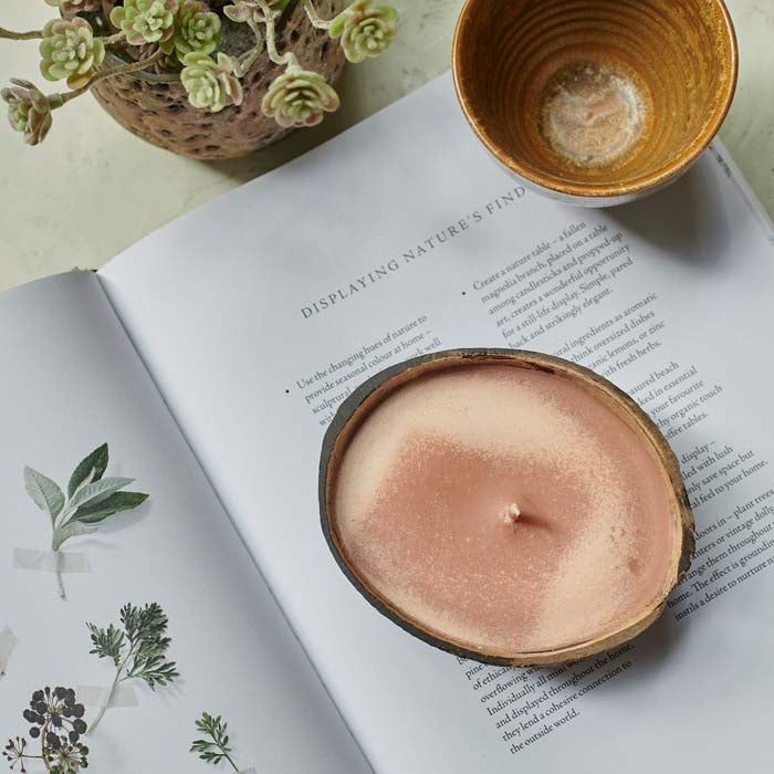 Orangey-pink coloured scented candle in a coconut shell sat on an open book