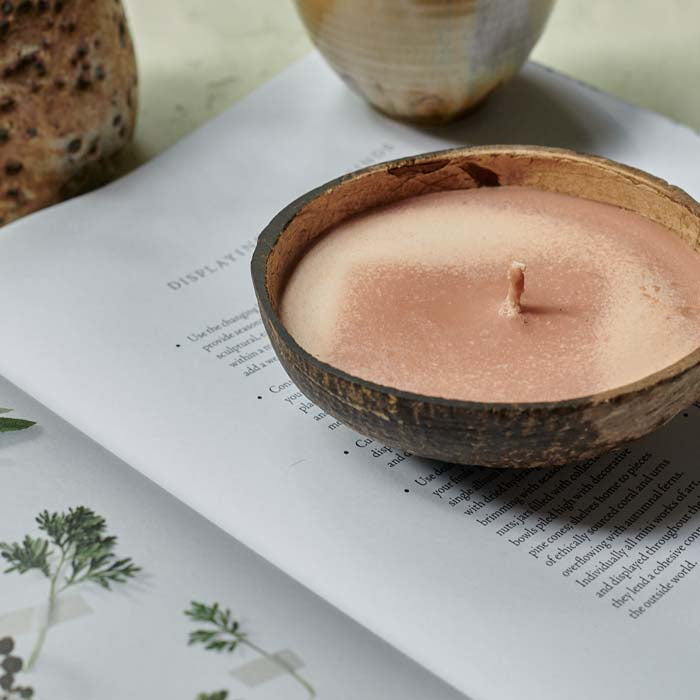 Orangey-pink coloured scented candle poured into a coconut shell sat on an open book