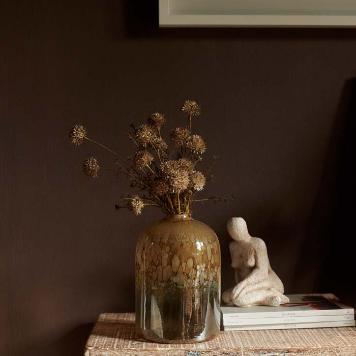 Two small faux flower stems placed in an amber and metallic grey glass vase on a wooden surface