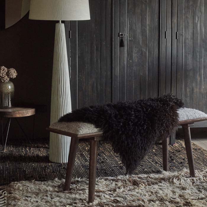 Black sheepskin draped over a wooden bench with a shaggy rug underneath