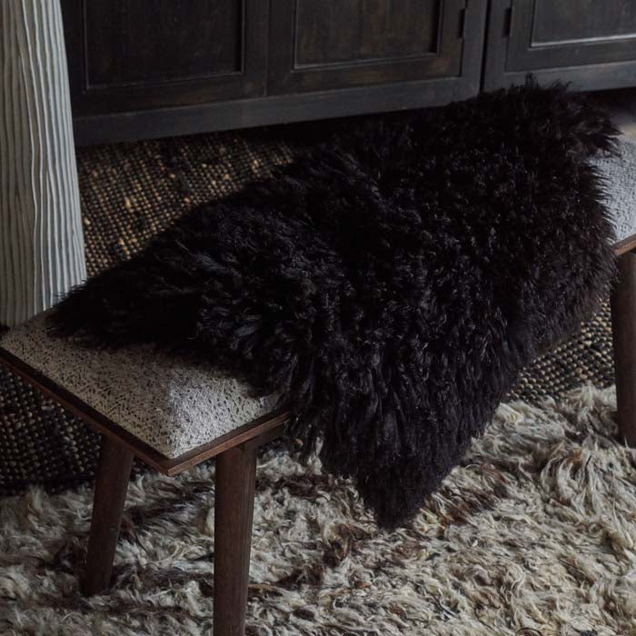 Black furry sheepskin draped over a dark brown bench