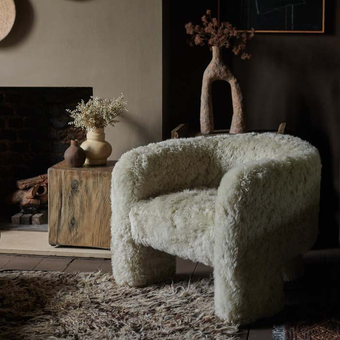 Furry cream sheepskin armchair sat on a brown shaggy rug in a living room