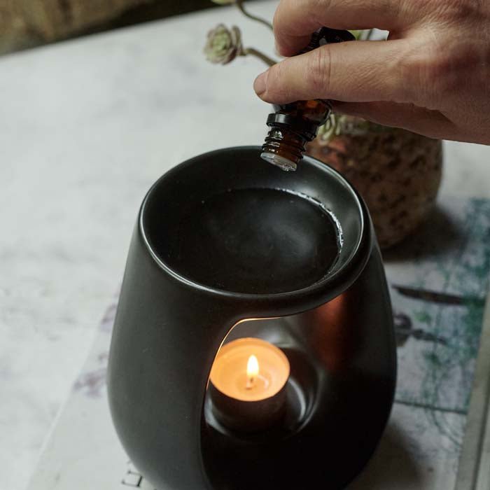 Fragrance oil being poured into a black ceramic oil burner with a lit tea light on its base