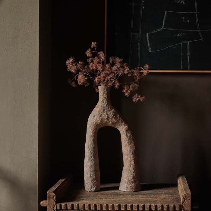Arched terracotta coloured vase filled with a faux bouquet of artificial foliage stems