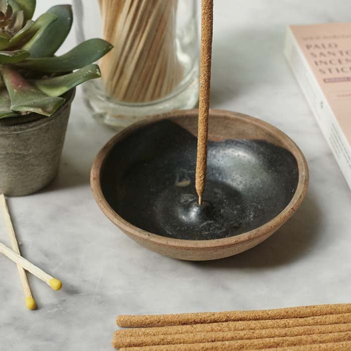 Round black incense holder with a brown rim and an incense placed on top