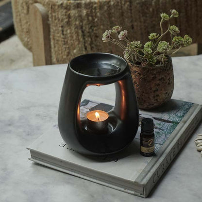Black ceramic oil burner with a lit tea light placed inside and fragrance oil on top