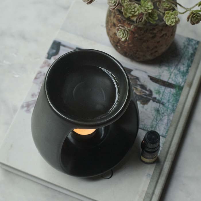 A lit tea light on the base of a black ceramic oil burner