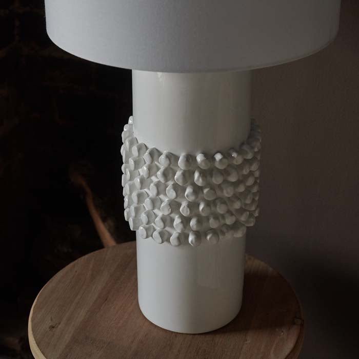 A close up of the Tavira Bobble Table Lamp. A smooth and bobbled white glazed ceramic base and a linen shade table lamp.