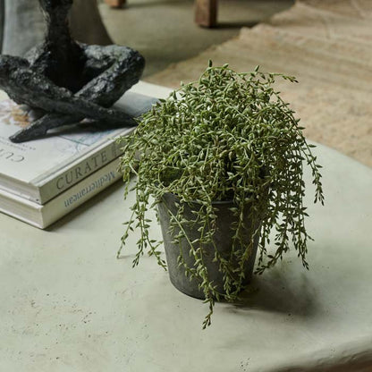 Textural artificial green plant in a tall, grey pot sat on a white coffee table