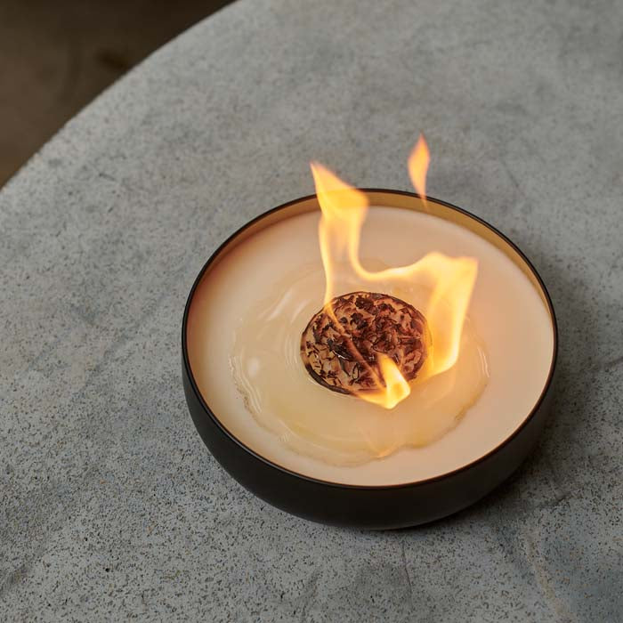 A large flame coming from a bonfire style scented candle in a black metal tin